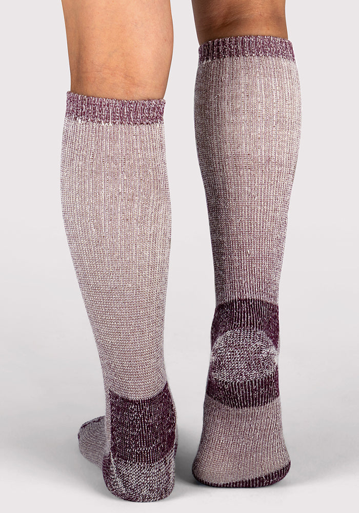 A person stands on a white background, shown from the back with their left calf and heel visible, wearing Woolx Womens Extreme Over The Calf Socks in Windsor Wine.